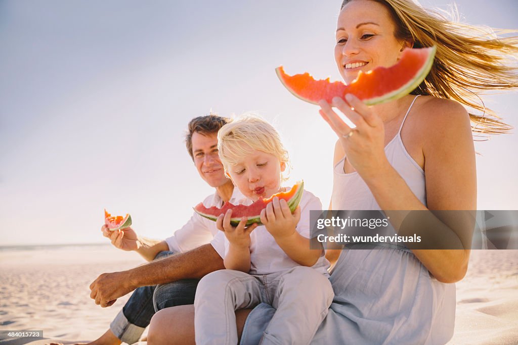 若い家族のビーチで食べるウォーターメロン