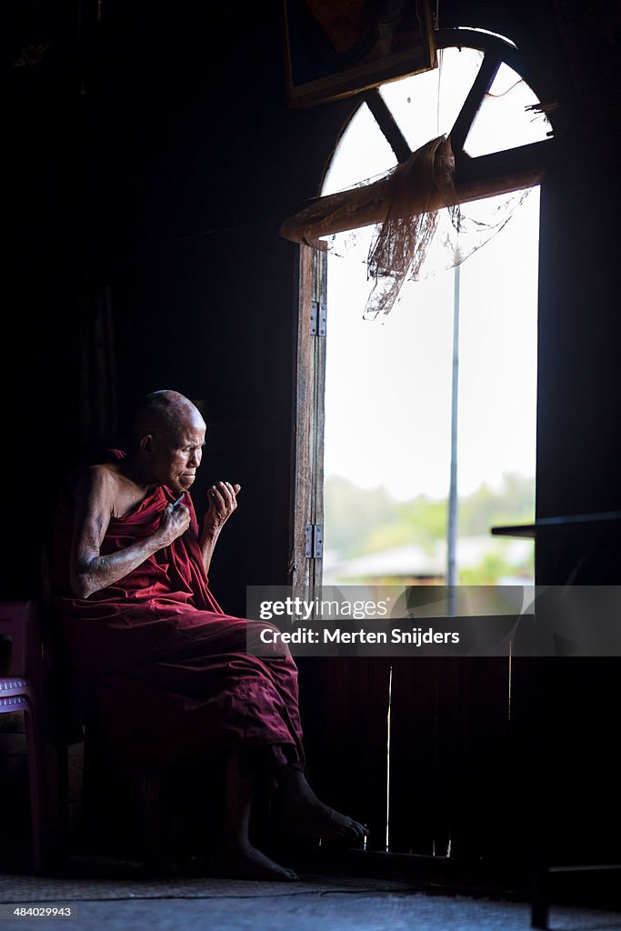 Buddhist monk shaving chin at window