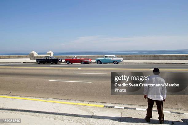 Cuban security guard stands in front of three US vintage cars at the Malecon waterfront next to the newly opened U.S. Embassy prior to the...