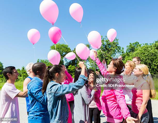 diverse group of survivors releasing balloons for breast cancer awarness - releasing balloons stock pictures, royalty-free photos & images