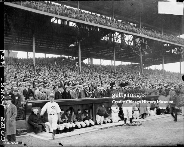 Chicago Cubs baseball players and managers in around the dugout in front of crowds in the grandstands at Wrigley Field, located at 1060 West Addison...