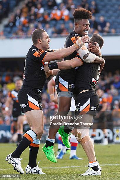 James Tedesco of the Tigers celebrates with team mates Robbie Farah and Kevin Naiqama after scoring a try during the round 23 NRL match between the...