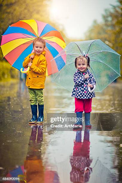 little boy and girl in rain - multi colored jacket stockfoto's en -beelden