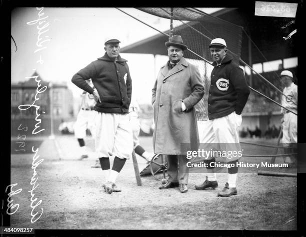 Chicago Cubs baseball player Alexander, co-owner William Wrigley Jr, and manager Bill Killefer standing behind a batting practice backstop on the...