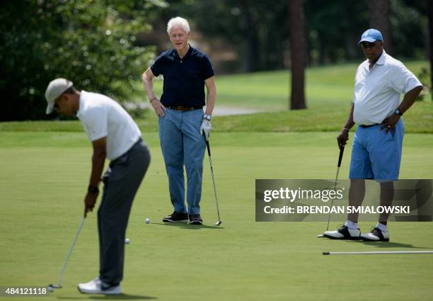 Former US President Bill Clinton and Ron Kirk watch as US President Barack Obama putts while golfing at Farm Neck Golf Club August 15, 2015 in Oak...