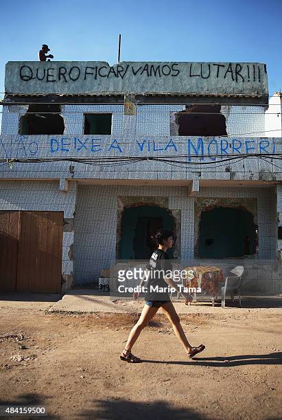 Teen stands on the rooftop of a partially demolished home in the Vila Autodromo 'favela' community, with graffiti reading 'I Want to Stay/Let's...