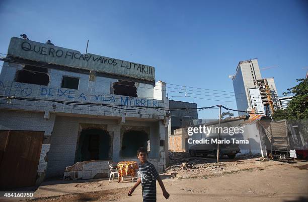 Teens stand on the rooftop of a partially demolished home in the Vila Autodromo 'favela' community, with Olympic Park construction rising in the...