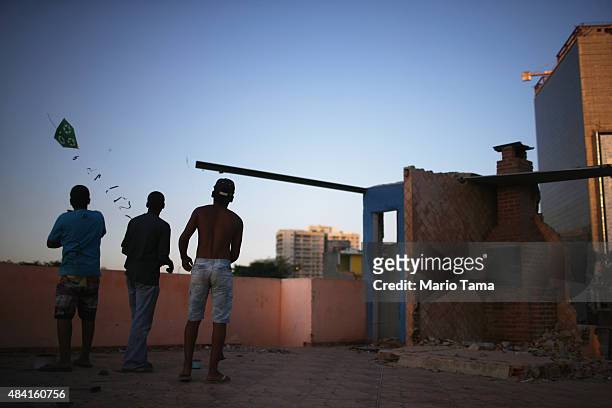 Teens fly kites on the rooftop of a partially demolished home in the Vila Autodromo 'favela' community, with a chimney remaining and Olympic Park...