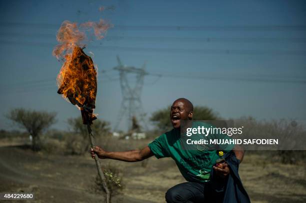 Mine worker burns a shirt on a torch during a ceremony marking the third anniversary of the Marikana massacre of 34 striking platinum miners, near...