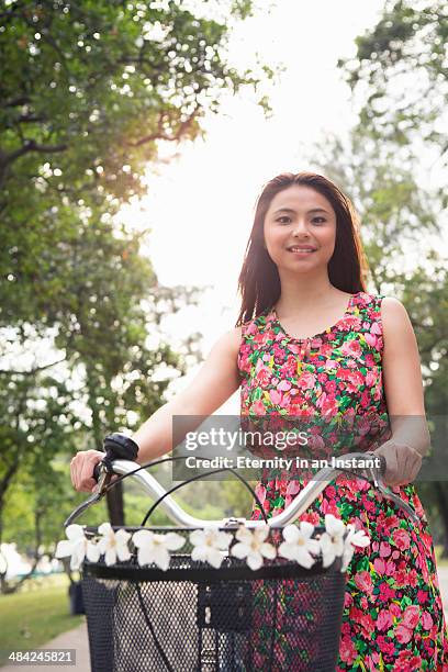 young woman pushing a bike, smiling.. - multi coloured dress stock-fotos und bilder