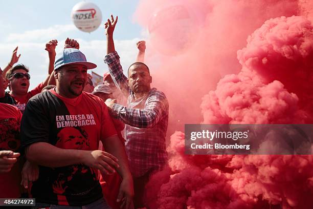 Demonstrators dressed in the colors of the Workers' Party stand next to smoke from a flare during a protest in Sao Paulo, Brazil, on Sunday, Aug. 16,...
