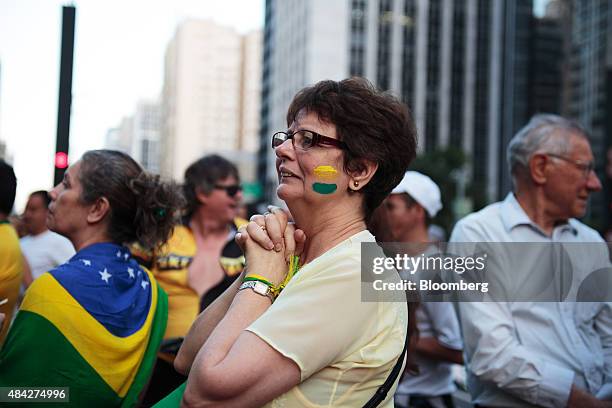 Demonstrator with the colors of the Brazilian flag painted on her face reacts during a protest in Sao Paulo, Brazil, on Sunday, Aug. 16, 2015....