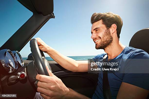 young man driving convertible by the sea - auto convertibile photos et images de collection