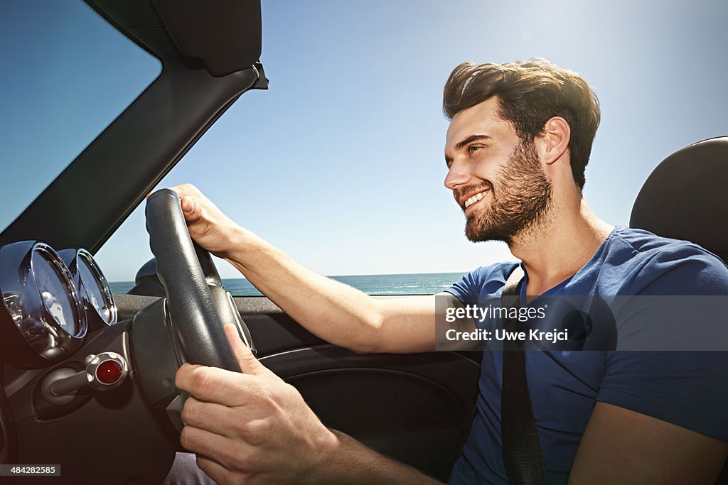 Young man driving convertible by the sea