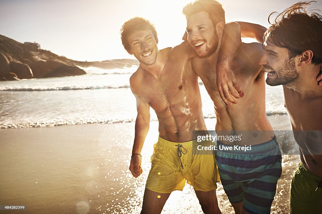 Three bare-chested men on beach, smiling, close-up