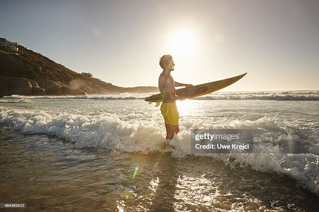 Young man carrying surfboard on Llandudno beach