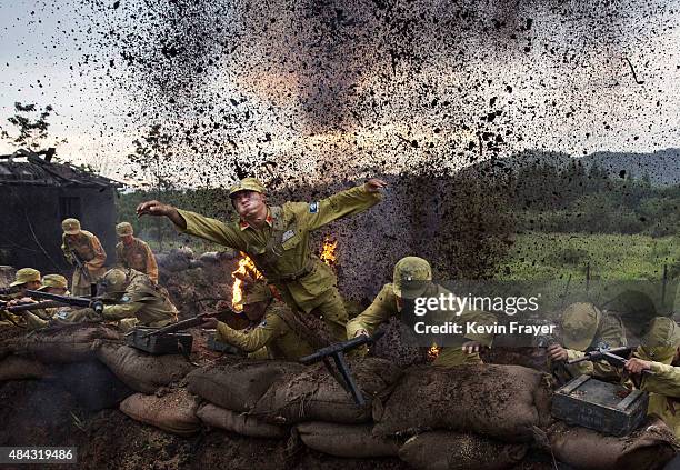 Chinese actor playing a Nationalist soldier leaps out of a tench in an explosion set-off by effects technicians during filming of a battle segment in...