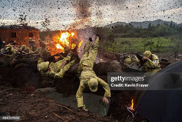 Chinese actors playing Nationalist soldiers leap out of a trench in an explosion set-off by effects technicians during filming of a battle segment in...