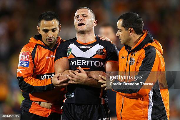 Robbie Farah of the Tigers is helped from the field after sustaining an injury to his elbow during the round 6 NRL match between the Wests Tigers and...