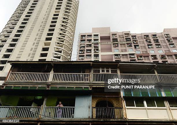 An Indian woman residing in a chawl - traditional old tenement for the working class - stands on her house balcony as a new high-rise tower and a...