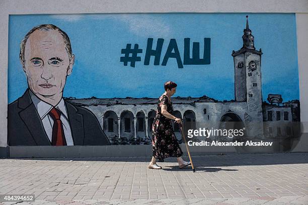 People walk by fresh graffiti depicting Vladimir Putin in Simferopol on August 17, 2015 in Simferopol, Crimea. Russian President Vladimir Putin...