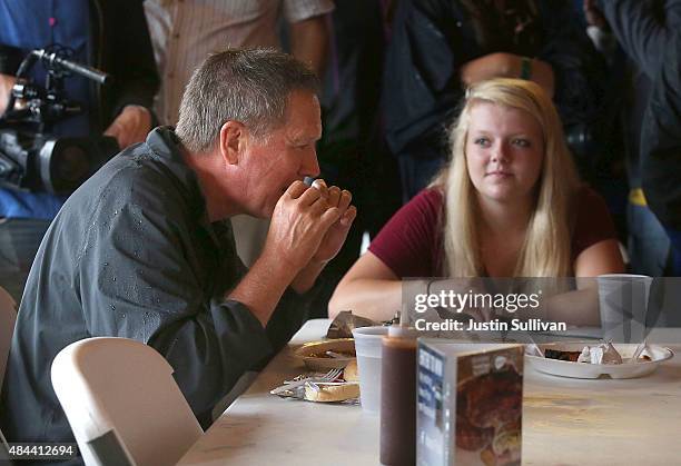 Republican presidential candidate and Ohio Gov. John Kasich eats a pork chop while visiting the Iowa Pork Producers Pork Tent during the Iowa State...