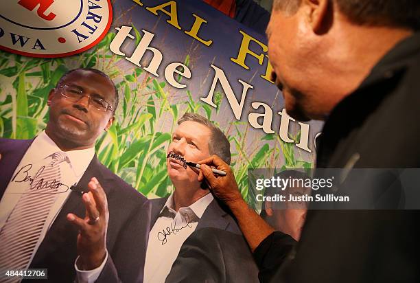 Republican presidential candidate and Ohio Gov. John Kasich draws a mustache on a picture of himself at the Republican Party of Iowa booth at the...