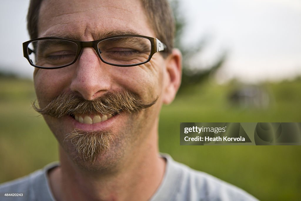 A mustached-man dons a smile in a field.