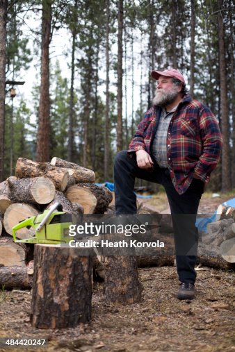 Portrait of rural man, chainsaw and wood pile.