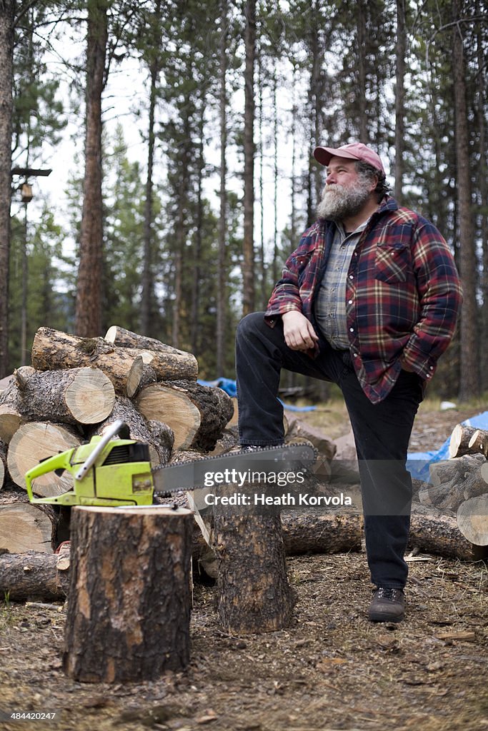 Portrait of rural man, chainsaw and wood pile.