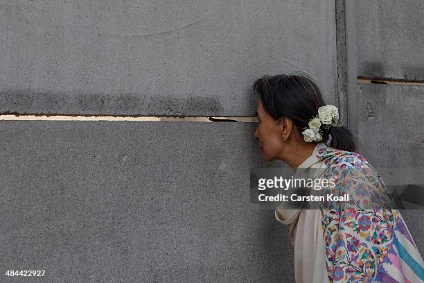 Myanmar pro-democracy leader Aung San Suu Kyi peeks through a crack in the back wall during a visit to the Berlin Wall Memorial on April 12, 2014 in...