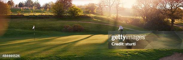 leuchtendes golfplatz mit golfspieler auf dem putting green - panorama stock-fotos und bilder