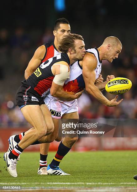 Scott Thompson of the Crows handballs whilst being tackled by Josh Saunders of the Saints during the round four AFL match between the St Kilda Saints...