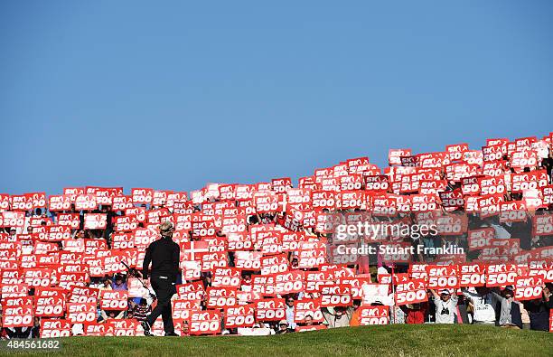 Soren Kjeldsen of Denmark walks onto the 16th green as fans hold placards to celebrate the 500th tournement during the first round of the Made in...