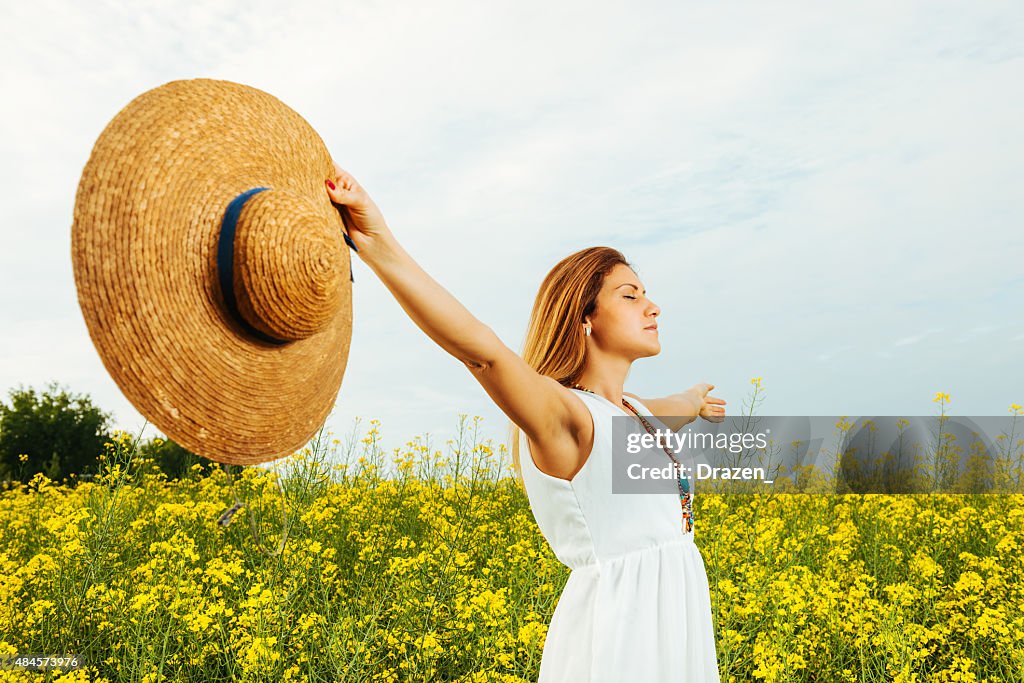 Beautiful woman with outstretching arms in yellow field in summer