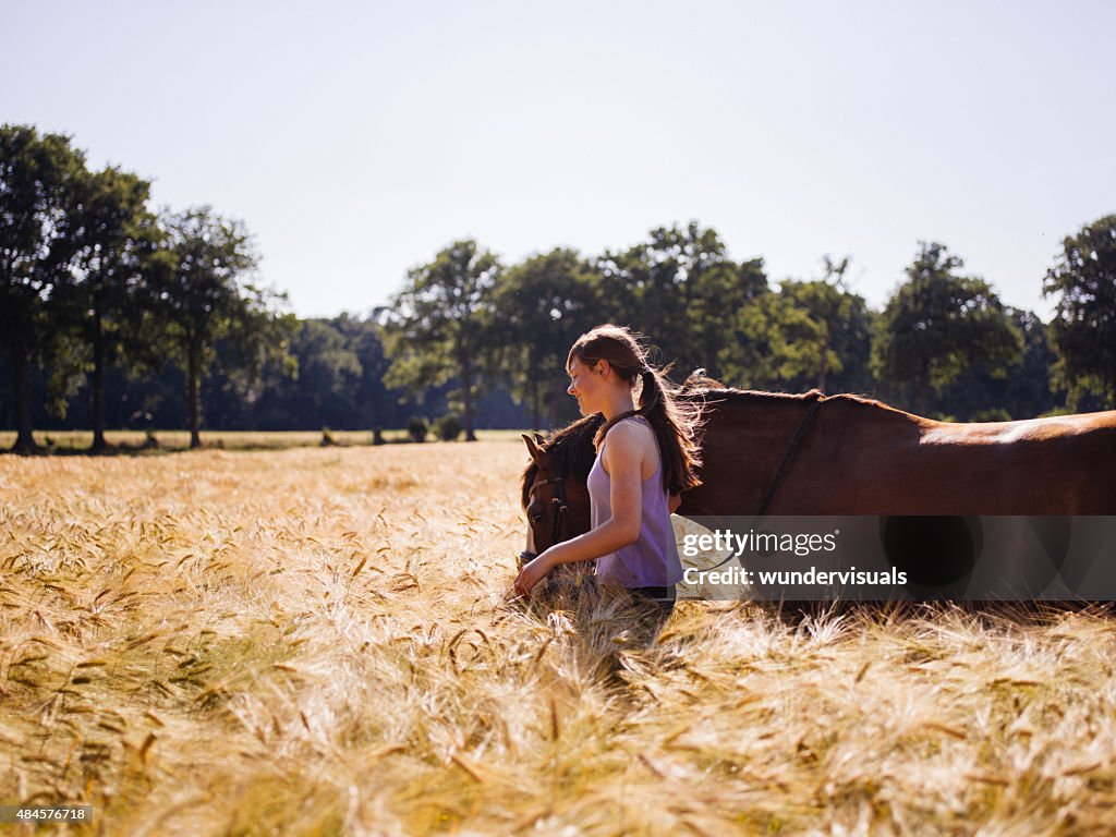 女性と彼女の馬を歩いて太陽の光が輝くウィイートフィールド