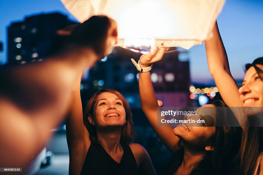 Friends on rooftop releasing paper lantern in the sky