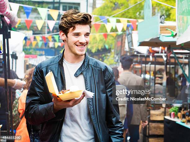 handsome british man walks through fair market with street food - food street market stock pictures, royalty-free photos & images