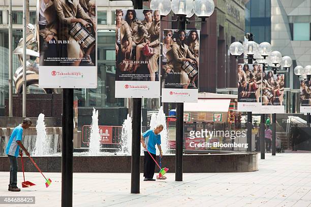 Cleaners sweep the street as Burberry Group Plc advertisements line the street outside the Takashimaya Co. Shopping mall on Orchard Road in Singapore...