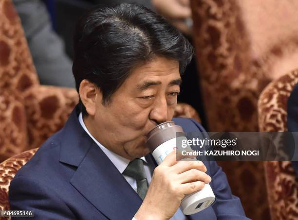 Japan's Prime Minister Shinzo Abe has a drink as he attends a special committee session in the upper house of parliament in Tokyo on August 21, 2015....