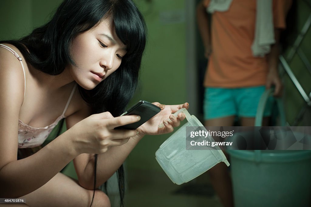 Teenage Asian girl using mobile phone while doing domestic works.