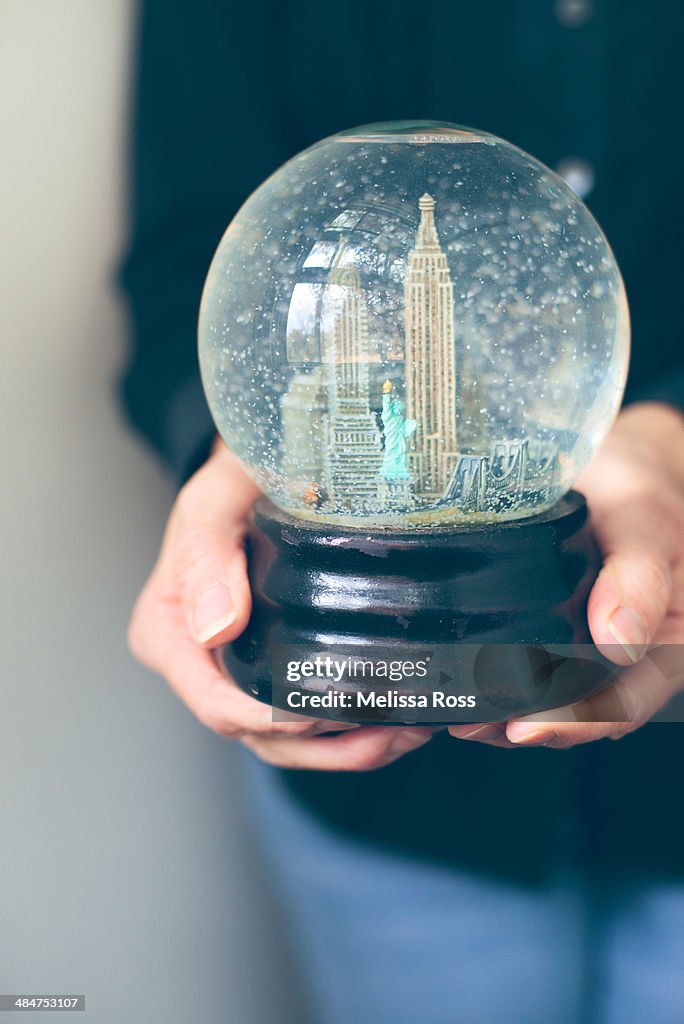 Hands holding a snow globe depicting New York City
