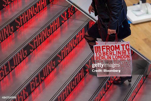 Customer holds a branded paper carrier bag as she walks up an illuminated staircase inside a Uniqlo store, the fashion clothing retailer operated by...