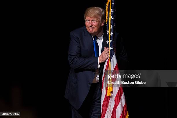 Republican presidential candidate Donald Trump hugs an American flag as he takes the stage for a town hall meeting in Derry, New Hampshire, August...