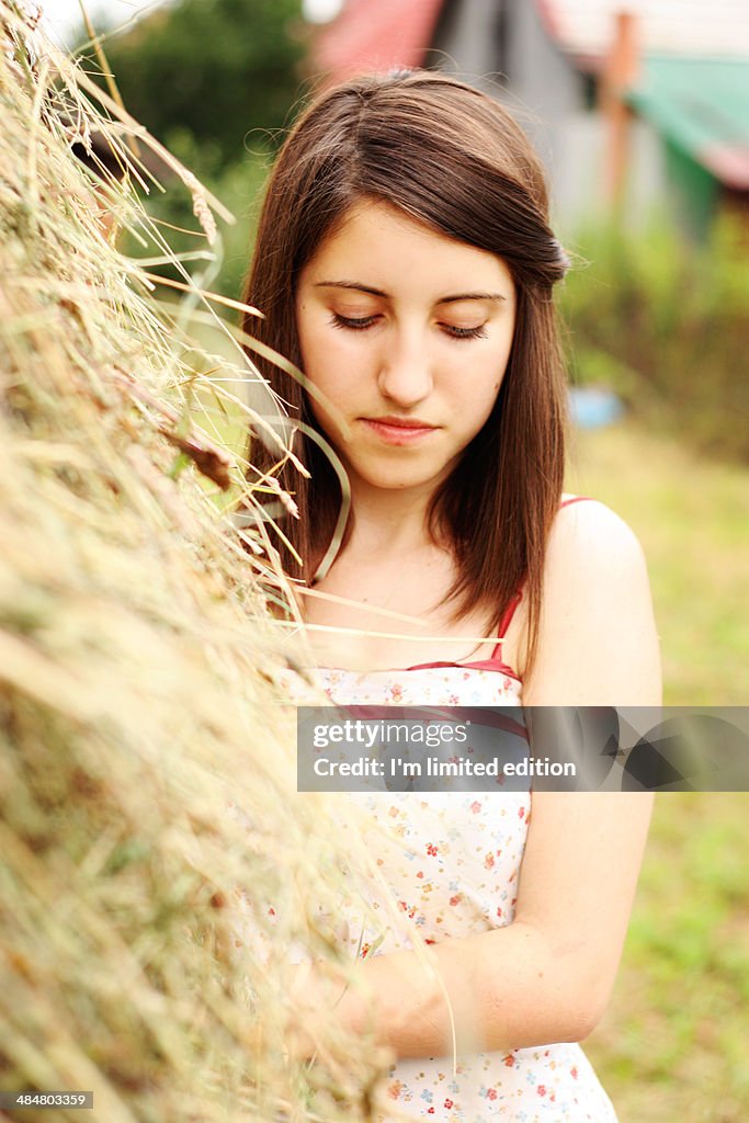 Girl standing next to a stack of hay being sad