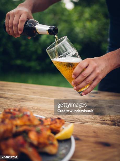 man pouring glass of beer with chicken wings in foreground - beer pour stock pictures, royalty-free photos & images