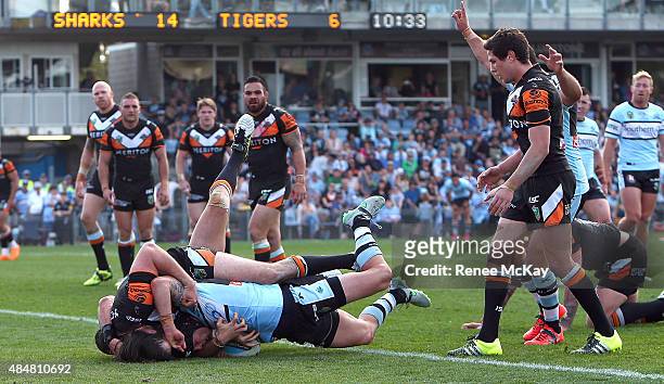 Michael Ennis of the Sharks scores a try in the tackle of Aaron Woods and James Tedesco of the Tigers during the round 24 NRL match between the...