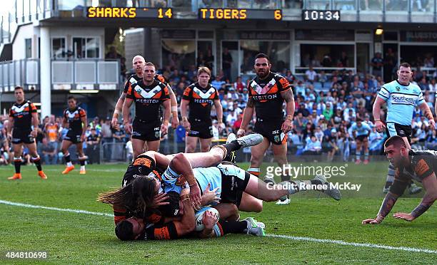 Michael Ennis of the Sharks scores a try in the tackle of Aaron Woods and James Tedesco of the Tigers during the round 24 NRL match between the...