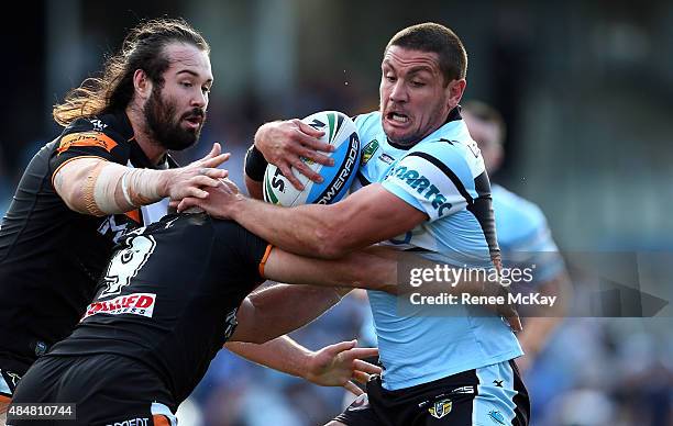 Chris Heighington of the Sharks is tackled by Aaron Woods and Robbie Farah of the Tigers during the round 24 NRL match between the Cronulla Sharks...