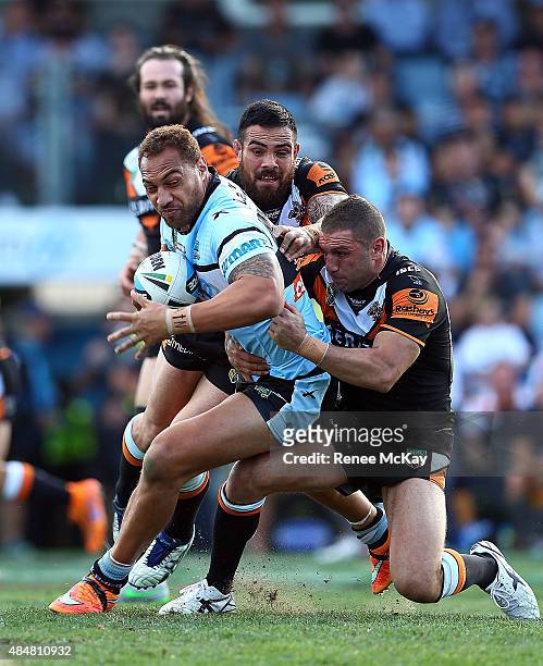Sam Tagataese of the Sharks is tackled by Dene Halatau and Robbie Farah of the Tigers during the round 24 NRL match between the Cronulla Sharks and...